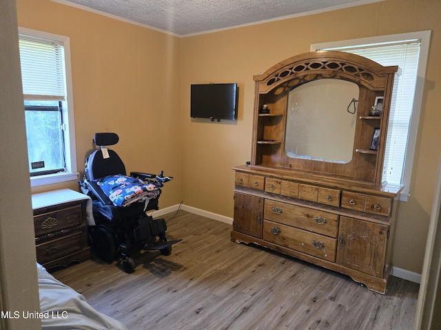 bedroom with light wood finished floors, a textured ceiling, baseboards, and crown molding