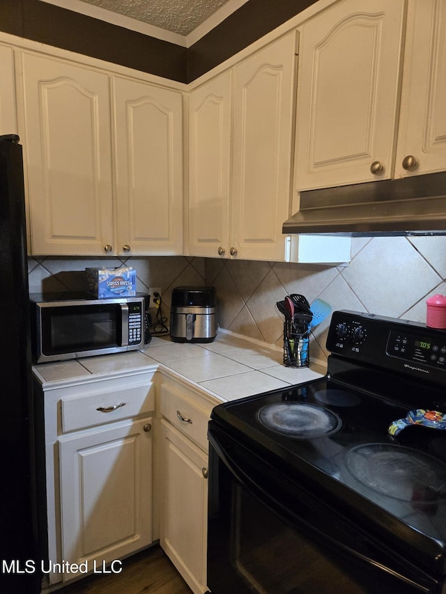 kitchen featuring black range with electric cooktop, under cabinet range hood, stainless steel microwave, and white cabinets