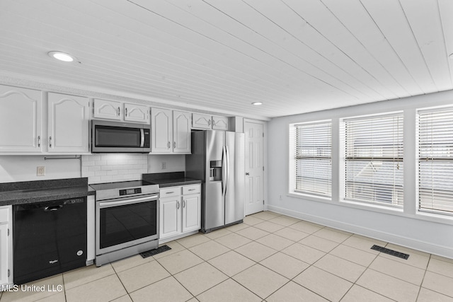 kitchen with light tile patterned floors, stainless steel appliances, dark countertops, visible vents, and backsplash