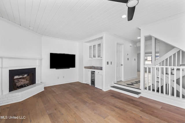 unfurnished living room featuring a dry bar, wood-type flooring, a fireplace with raised hearth, beverage cooler, and stairs