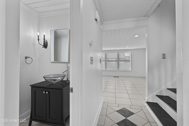 hall with ornamental molding, tile patterned flooring, a sink, and baseboards