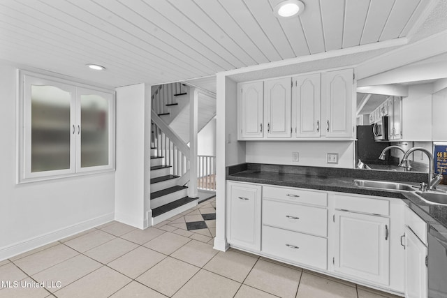 kitchen featuring dark countertops, stainless steel microwave, a sink, and white cabinetry