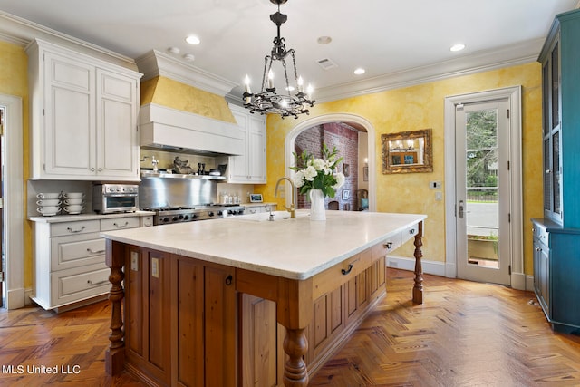 kitchen featuring white cabinetry, parquet flooring, a center island with sink, and hanging light fixtures