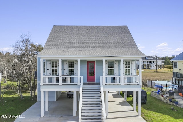 beach home featuring stairway, roof with shingles, a porch, a carport, and a front lawn