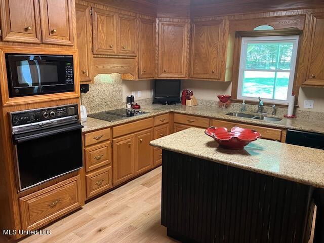 kitchen with light stone countertops, a kitchen island, black appliances, light wood finished floors, and a sink