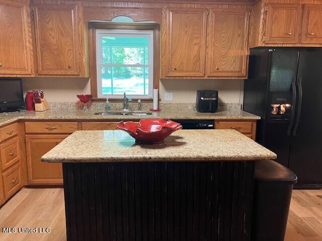 kitchen with black appliances, light wood-style floors, a kitchen island, and a sink