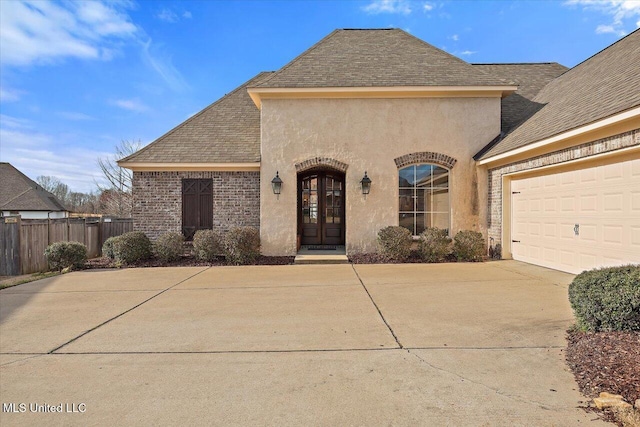 view of front of property with french doors, stucco siding, a shingled roof, concrete driveway, and fence