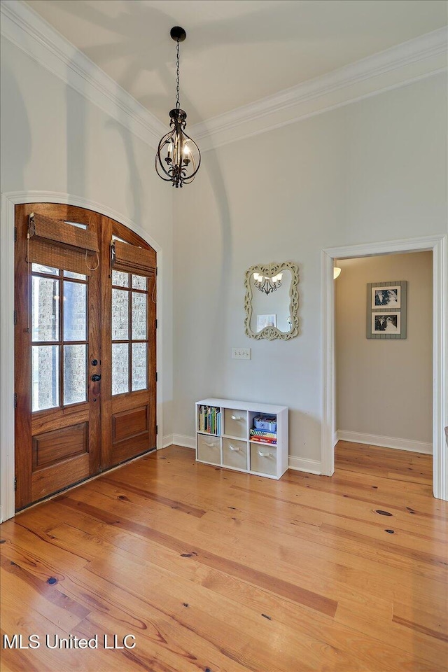 foyer with crown molding, baseboards, french doors, light wood finished floors, and an inviting chandelier