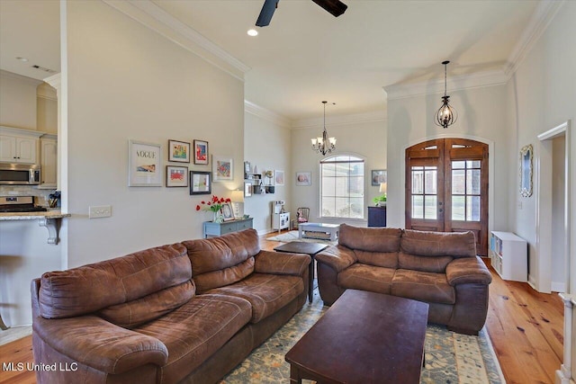 living room with arched walkways, ceiling fan with notable chandelier, french doors, ornamental molding, and light wood finished floors