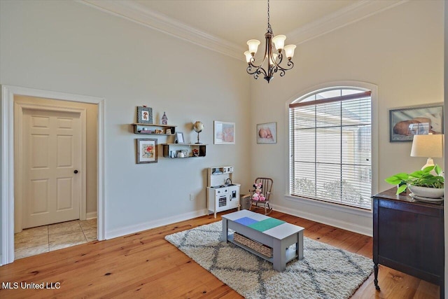 sitting room with baseboards, ornamental molding, an inviting chandelier, and light wood-style floors