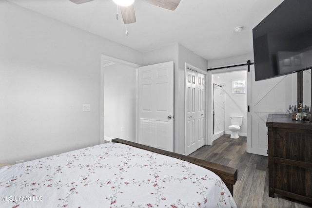 bedroom featuring a closet, a barn door, ceiling fan, dark hardwood / wood-style flooring, and ensuite bathroom