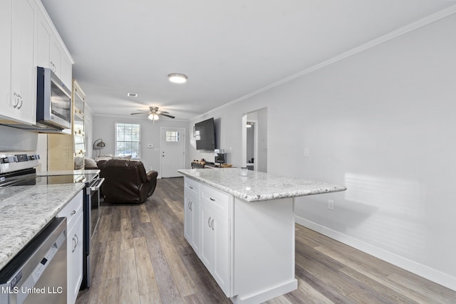 kitchen with stainless steel appliances, a center island, crown molding, ceiling fan, and white cabinetry