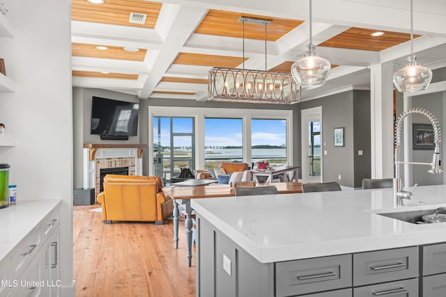 kitchen featuring hanging light fixtures, light wood-type flooring, gray cabinets, light stone counters, and coffered ceiling