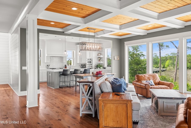 living room with beamed ceiling, coffered ceiling, dark hardwood / wood-style floors, and an inviting chandelier