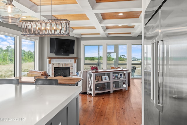 kitchen with wood-type flooring, a brick fireplace, beamed ceiling, decorative light fixtures, and coffered ceiling