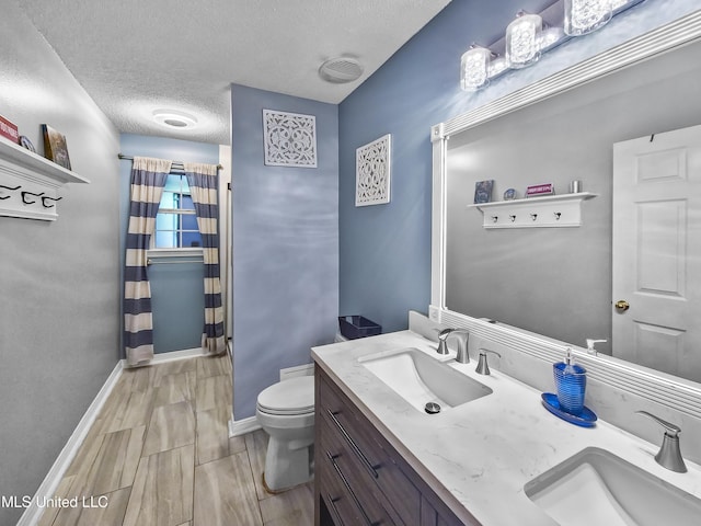 11295 Peyton Dr, Gulfport, MS 39503 - bathroom featuring toilet, a textured ceiling, baseboards, wood finish floors, and double vanity