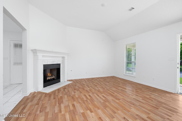 unfurnished living room featuring light wood finished floors, a fireplace, visible vents, baseboards, and lofted ceiling