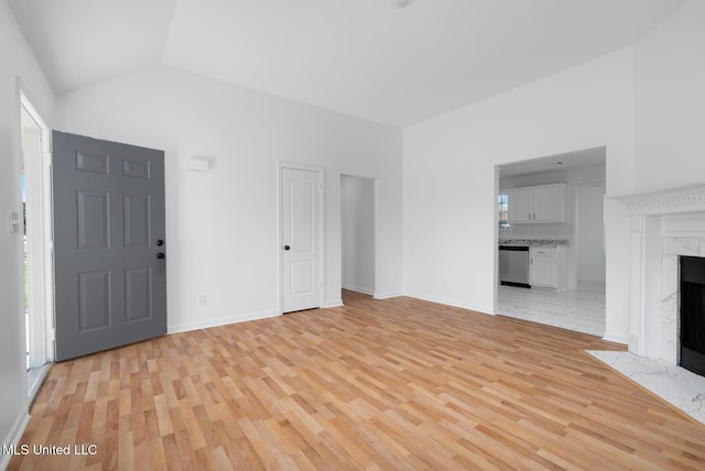 unfurnished living room featuring a premium fireplace, lofted ceiling, light wood-style flooring, and baseboards