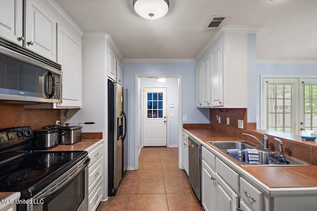 900 Redwood Cv, Byram, MS 39272 - kitchen featuring appliances with stainless steel finishes, white cabinets, backsplash, crown molding, and light tile patterned floors