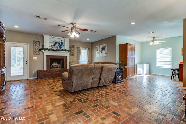 living room featuring a textured ceiling, a wealth of natural light, and a brick fireplace