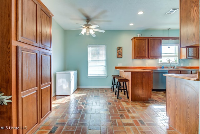 kitchen featuring ceiling fan, sink, stainless steel dishwasher, decorative light fixtures, and a kitchen bar