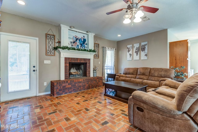 living room with ceiling fan, a fireplace, and a textured ceiling