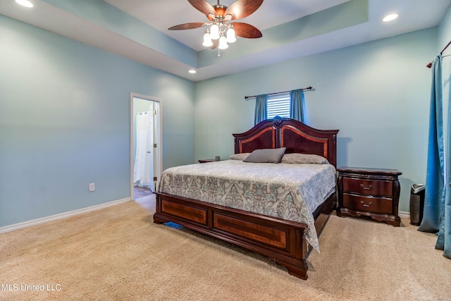 carpeted bedroom with ensuite bathroom, a raised ceiling, and ceiling fan