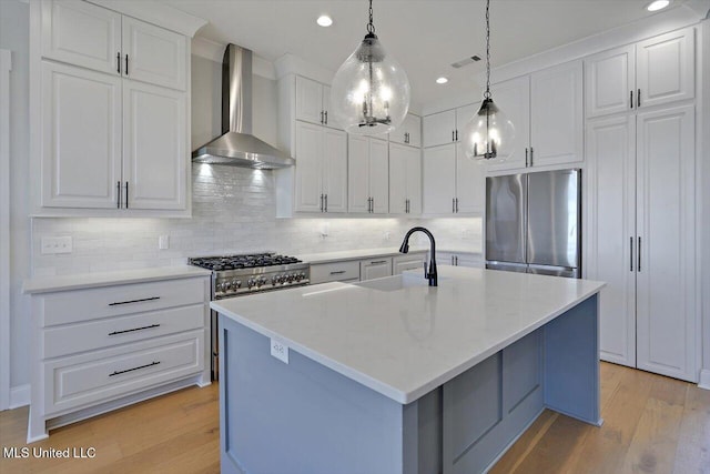 kitchen featuring wall chimney exhaust hood, light wood-style flooring, freestanding refrigerator, white cabinetry, and a sink