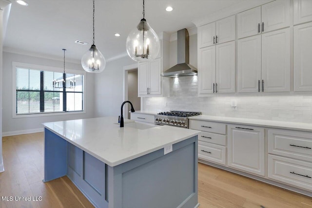 kitchen featuring stainless steel stove, a sink, light countertops, ornamental molding, and wall chimney exhaust hood