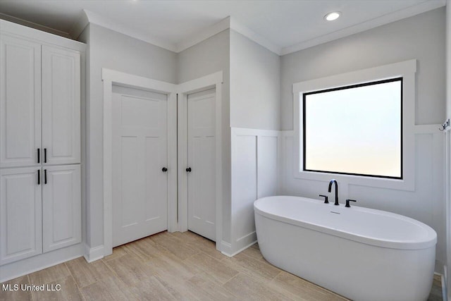 bathroom with a freestanding tub, crown molding, wood finished floors, and a wainscoted wall