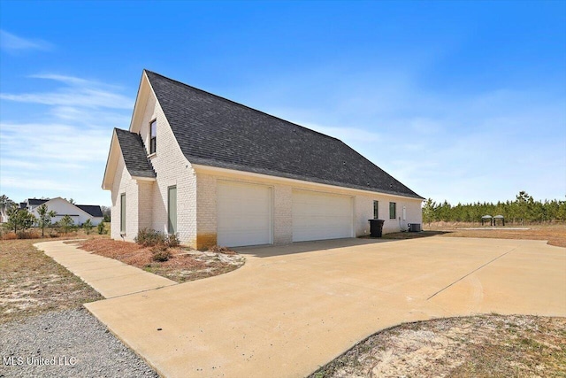 view of home's exterior with brick siding, a shingled roof, central AC, a garage, and driveway