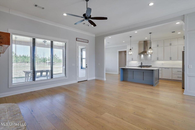 kitchen featuring white cabinets, light countertops, ornamental molding, light wood-type flooring, and wall chimney exhaust hood