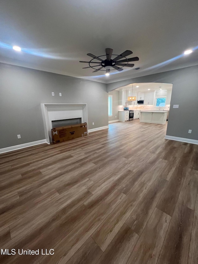 unfurnished living room featuring ceiling fan and dark wood-type flooring