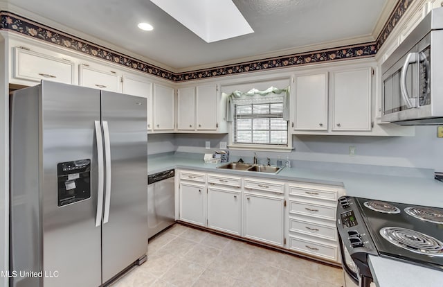 kitchen featuring a skylight, white cabinets, appliances with stainless steel finishes, light countertops, and a sink