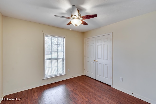 unfurnished bedroom with ceiling fan, a closet, baseboards, and dark wood-style flooring