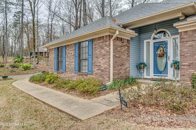 entrance to property with roof with shingles and brick siding