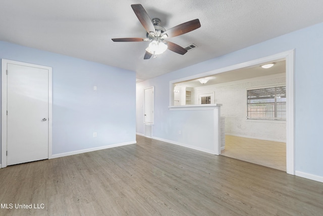 unfurnished living room featuring wood-type flooring, brick wall, ceiling fan, and a textured ceiling