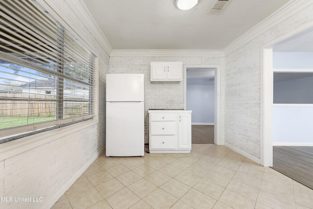 kitchen with light tile patterned floors, white cabinetry, ornamental molding, brick wall, and white fridge