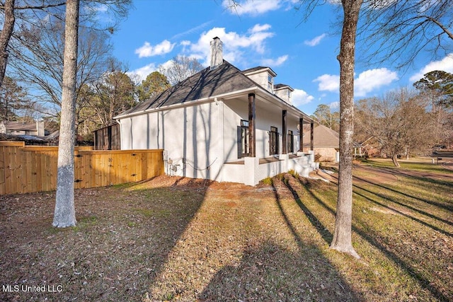 view of side of property with brick siding, a chimney, a yard, and fence