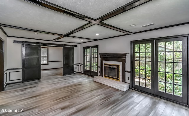 unfurnished living room with a wealth of natural light, a barn door, a brick fireplace, and wood-type flooring