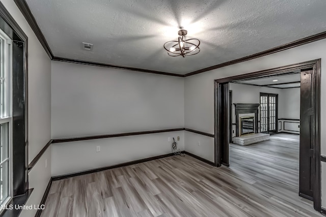 empty room featuring crown molding, a textured ceiling, and light wood-type flooring