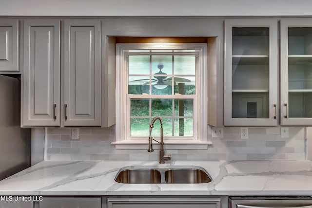 kitchen featuring stainless steel dishwasher, decorative backsplash, light stone countertops, and sink