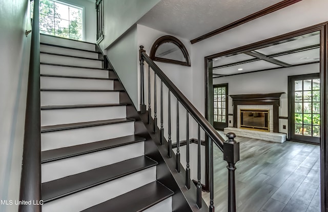 stairway with crown molding, a healthy amount of sunlight, a textured ceiling, and hardwood / wood-style floors