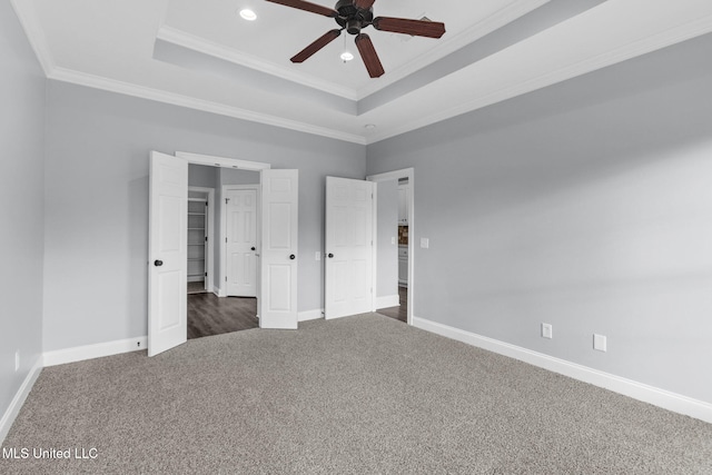 unfurnished bedroom with baseboards, a raised ceiling, crown molding, and dark colored carpet