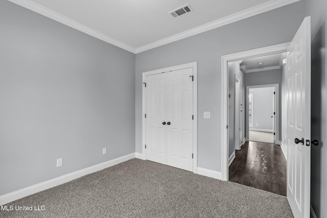 unfurnished bedroom featuring visible vents, baseboards, dark colored carpet, crown molding, and a closet