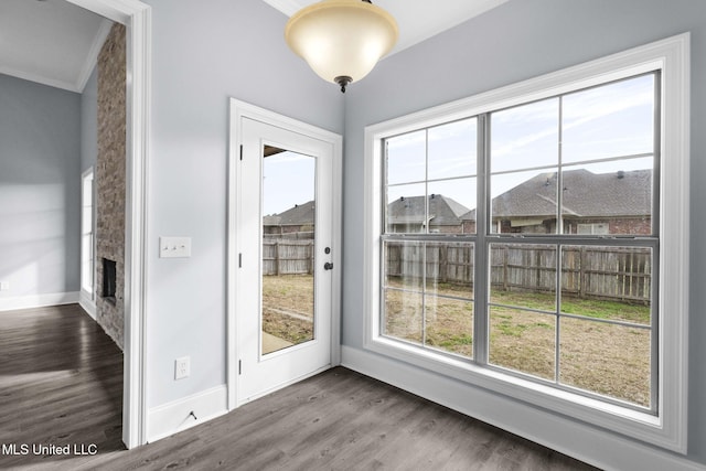 doorway with dark wood-type flooring, a large fireplace, crown molding, and baseboards