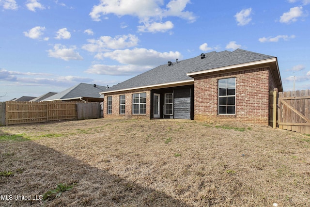 back of property featuring a fenced backyard, roof with shingles, and brick siding