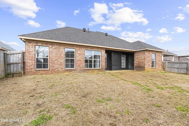 back of property featuring a yard, a fenced backyard, roof with shingles, and brick siding