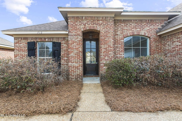 doorway to property featuring roof with shingles and brick siding