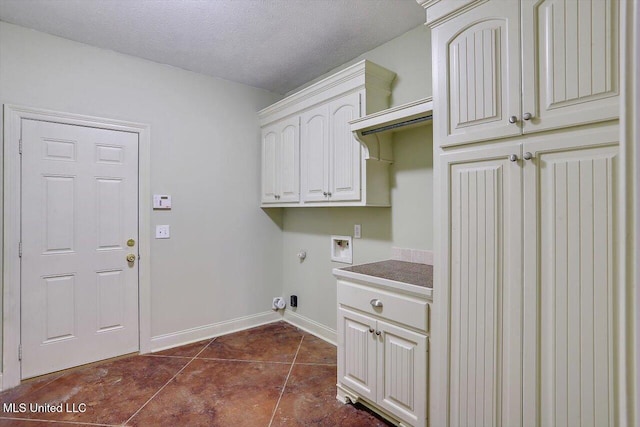 laundry area with a textured ceiling, hookup for a washing machine, cabinets, and dark tile patterned flooring